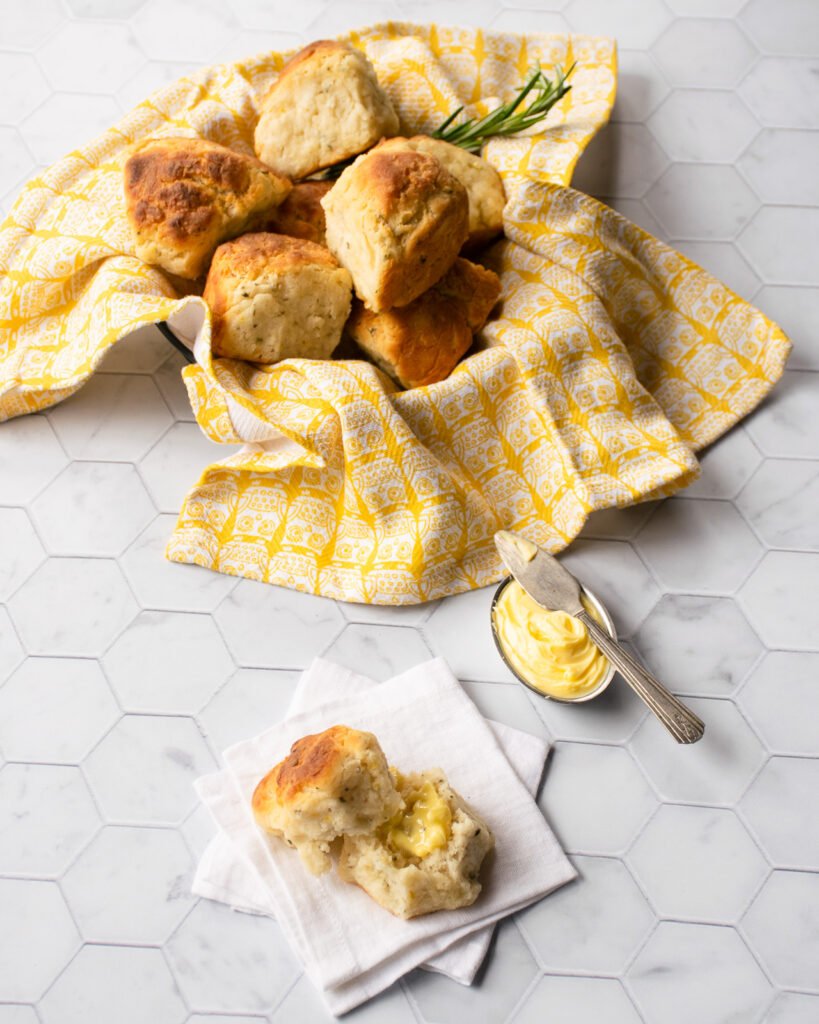 A basket of lemon rosemary biscuits lined with a yellow cloth with one broken open in front.