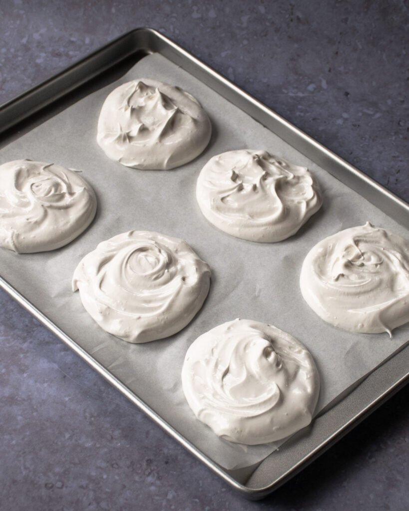 Raw pavlovas on parchment paper on a baking sheet.
