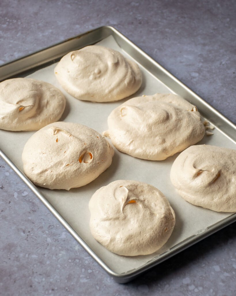 Cooked pavlovas on parchment paper on a baking sheet.