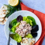 Salmon Salad on a bed of greens with some water crackers, lemon and dill and an orange napkin.