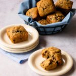 A blue napkin-lined basket with banana chocolate muffins inside and two plates with muffins.