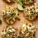 Chicken Tostadas on a wooden board with lime wedges and cilantro leaves.