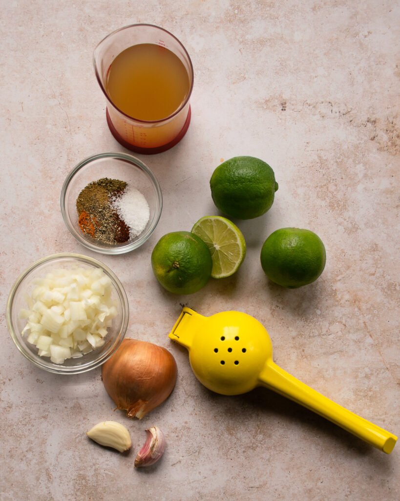 Ingredients on a counter - spices, limes, onion and stock.