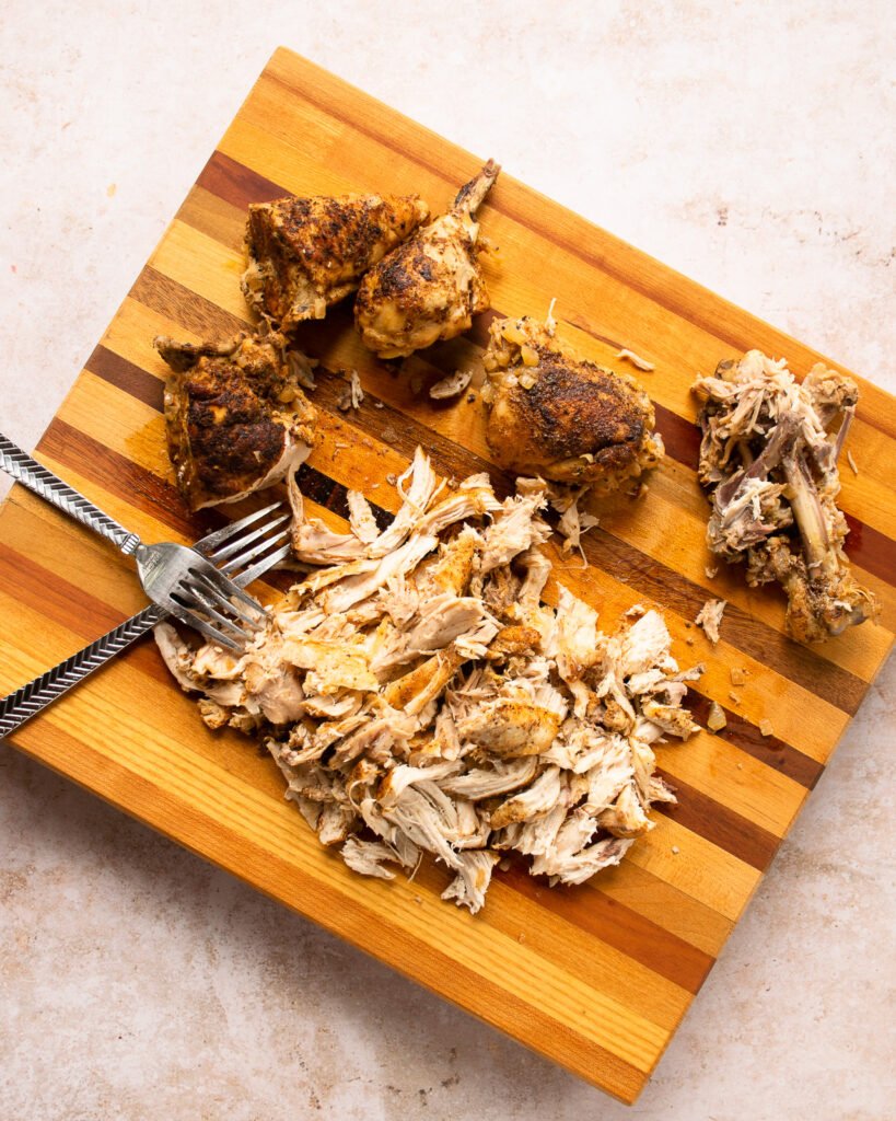Chicken being shredded on a cutting board with two forks.