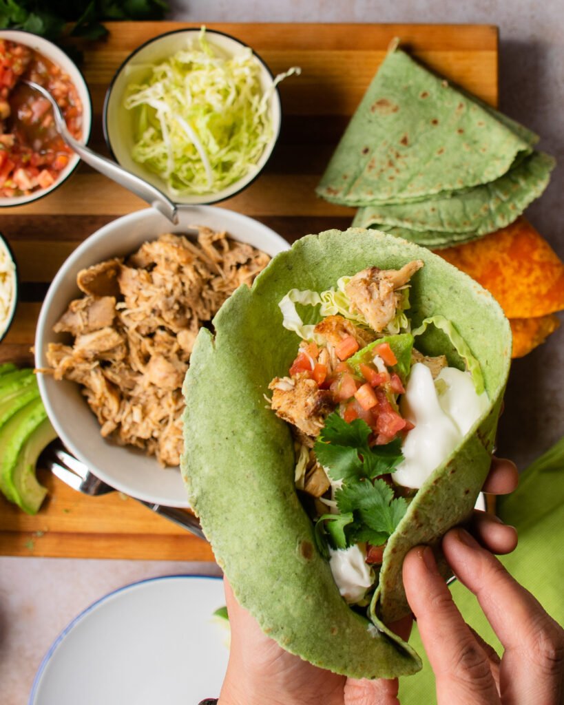 A chicken taco being wrapped up near all the ingredients.