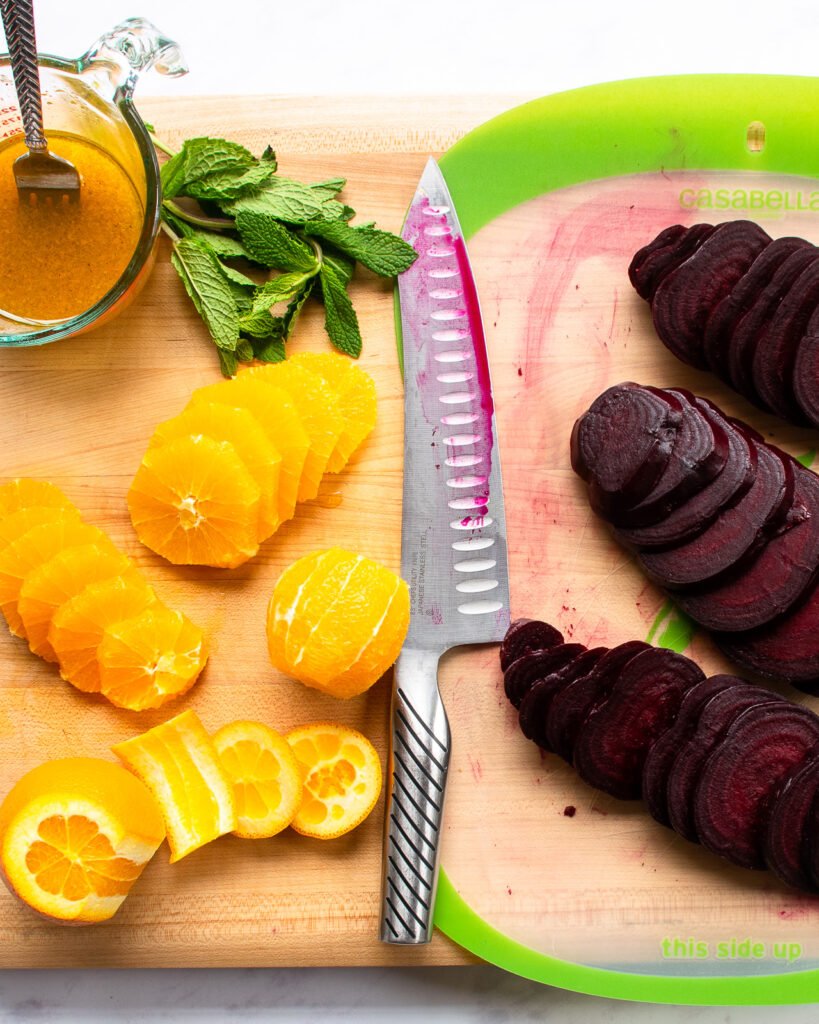 Oranges sliced, beets sliced and a knife on a wooden cutting board.