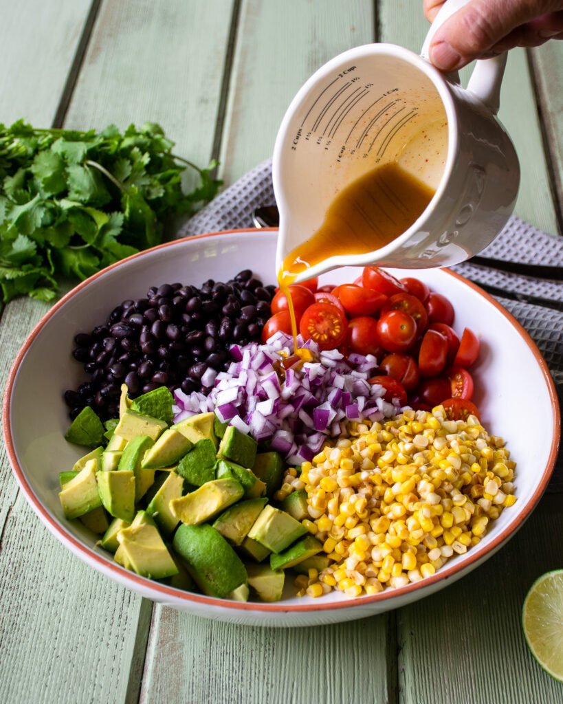 Dressing avocado tomato salad by pouring dressing over the top.