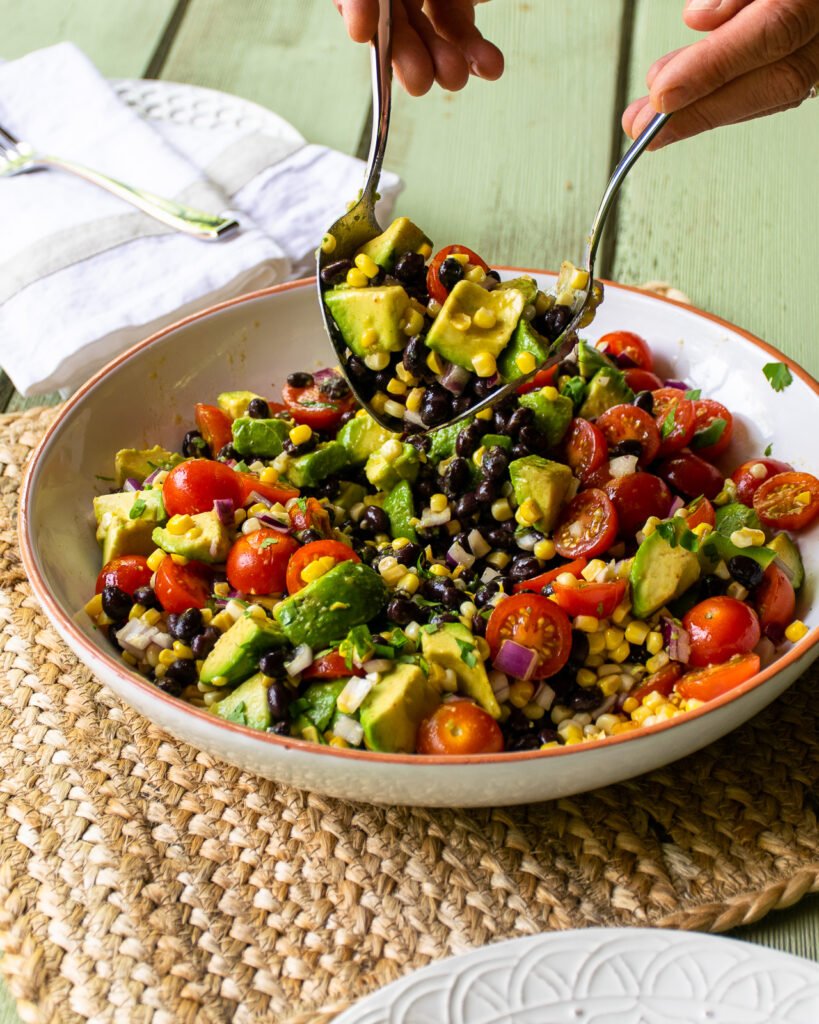 Salad servers lifting salad out of a salad bowl.