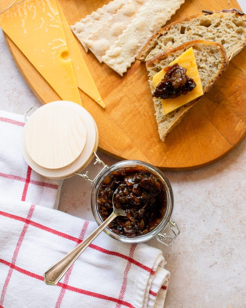 Bacon Jam Bacon jam in a jar with a spoon sticking out of it and a piece of bread with cheese and bacon jam.