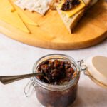 A jar of bacon jam with a cheese board in the background.