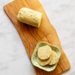 A log of gorgonzola shallot butter on a wooden board with a small green dish with slices of butter on the other end.