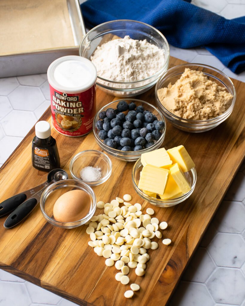 Ingredients on a wooden cutting board with a cake pan and a blue towel in the background.