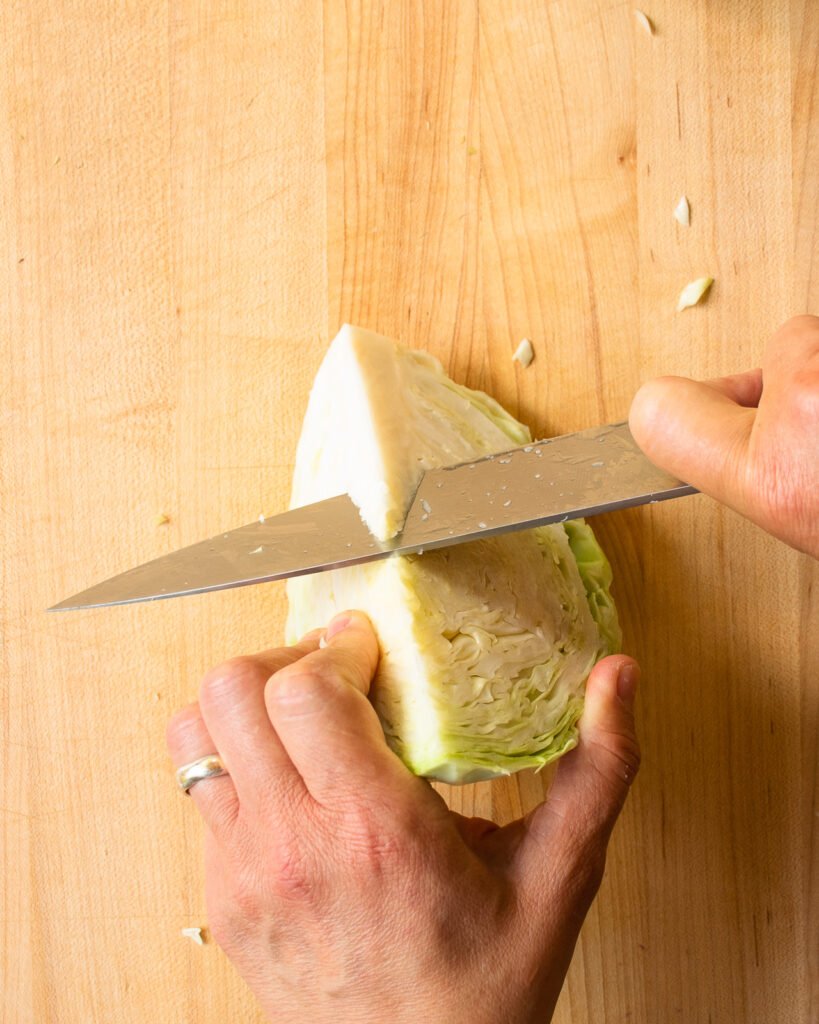 Two hands cutting the core off a quarter head of cabbage.