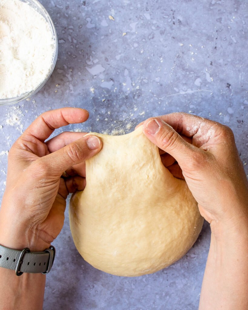 Two hands stretching dough thin to show when the dough has been kneaded enough.