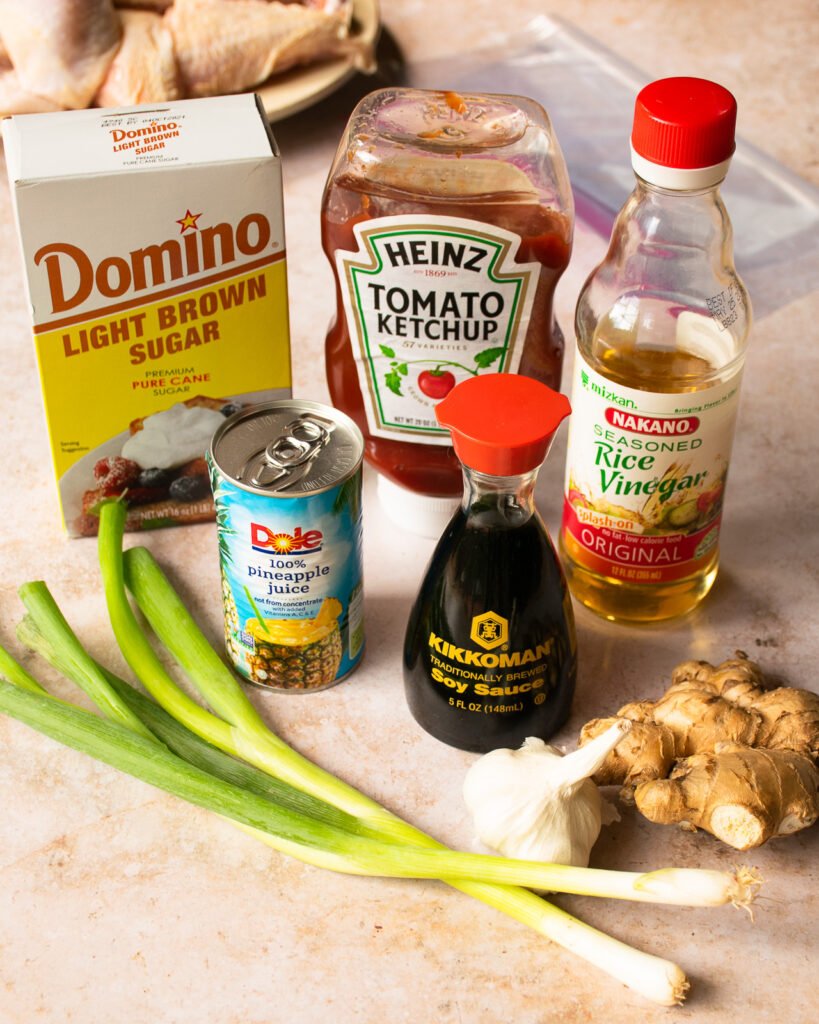 Ingredients on a countertop - brown sugar, ketchup, rice wine vinegar, pineapple juice, soy sauce, ginger, garlic and scallions.