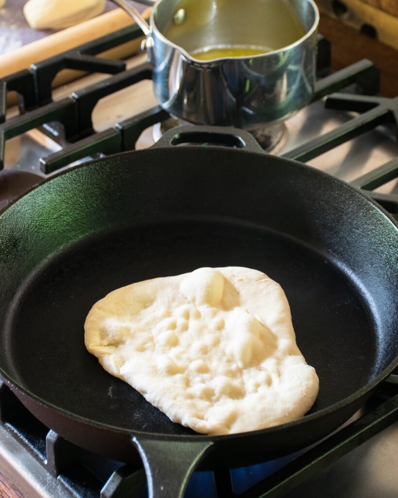 Naan bread cooking in a dry cast iron skillet.