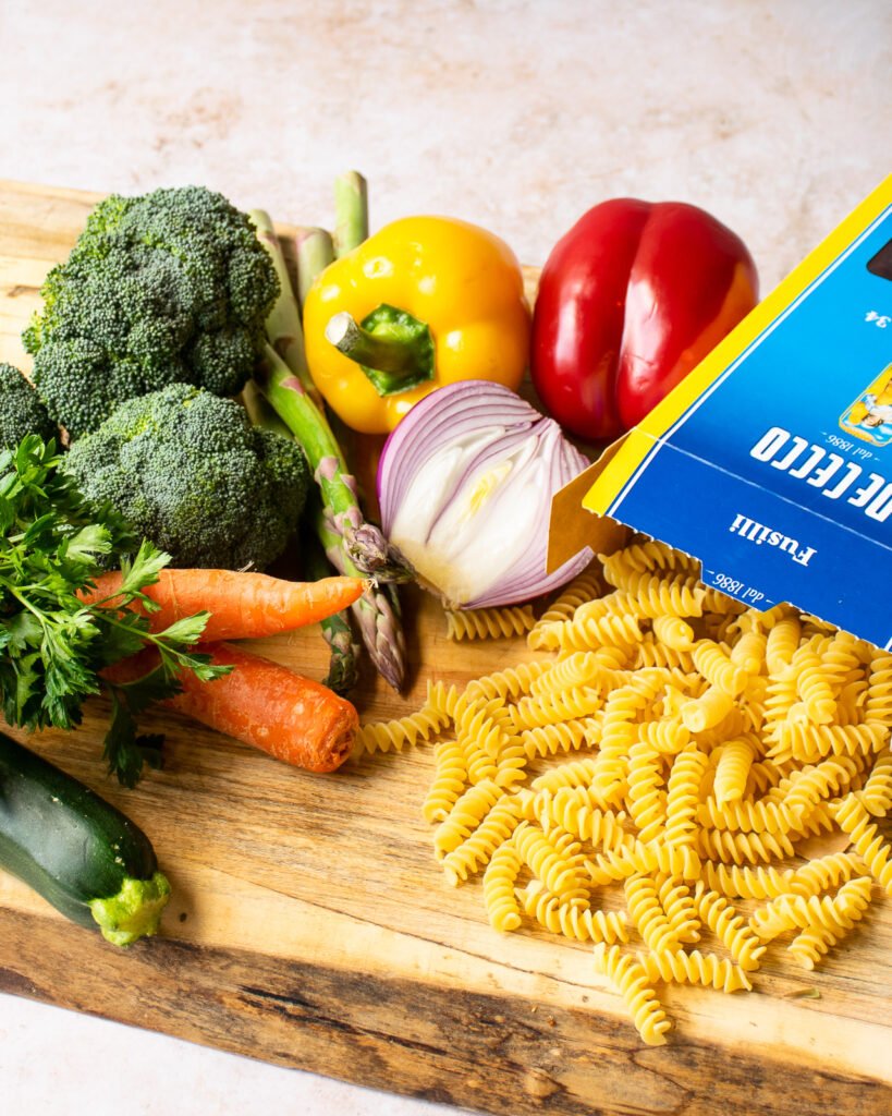 Ingredients on a wooden cutting board - pasta, vegetables.