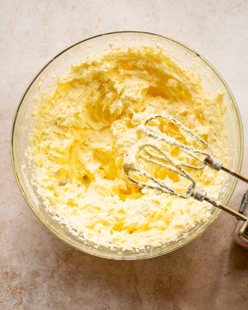 Creamed butter in a glass bowl with a hand mixer.