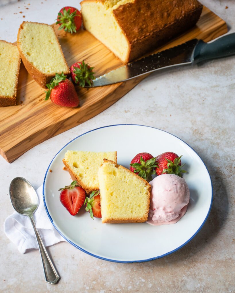 A piece of pound cake on a plate with some berries and a scoop of strawberry ice cream.