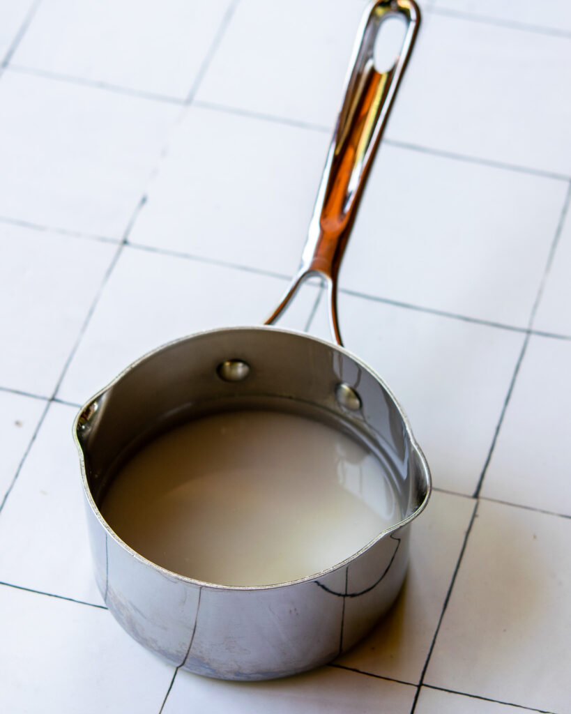 A saucepan with water and sugar inside on a tiled counter.