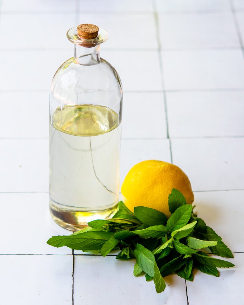 A bottle of simple syrup with a lemon and some mint leaves on a tiled counter.