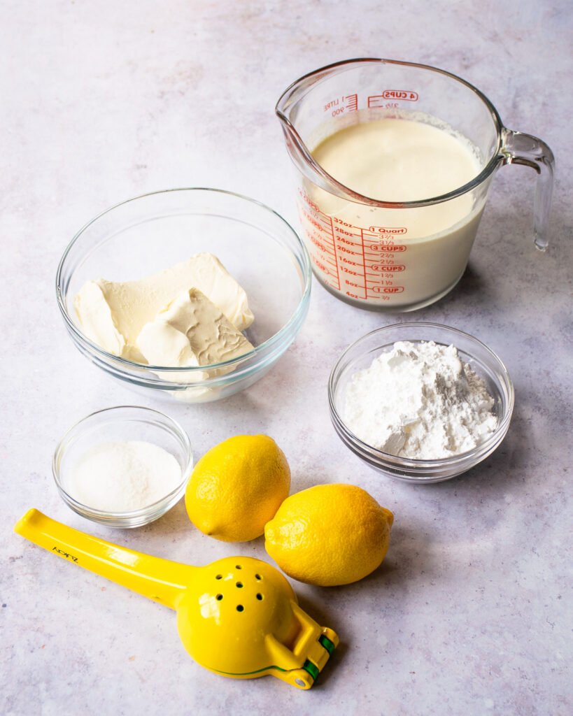 Ingredients on a countertop - cream, cream cheese, sugar, lemon and powdered sugar.