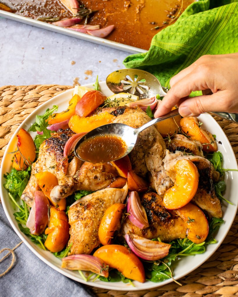 A hand spooning juice over chicken on a white platter.