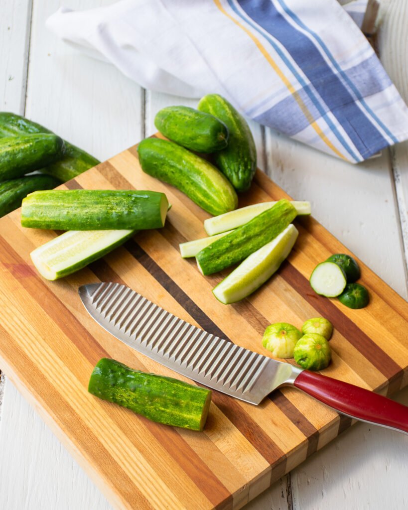 Cucumbers trimmed on a cutting board with a red handled knife.