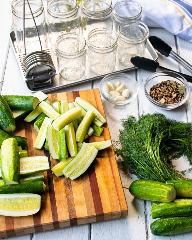 Cucumbers, dill, pickling spice and empty pint and quart jars on a table.