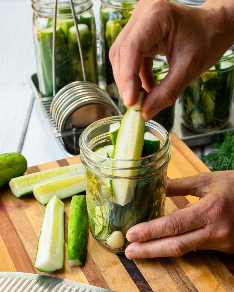 Hands packing cucumbers into jars for dill pickles.