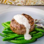 Filet Mignon with horseradish cream sitting on a bed of green beans on a blue plate.