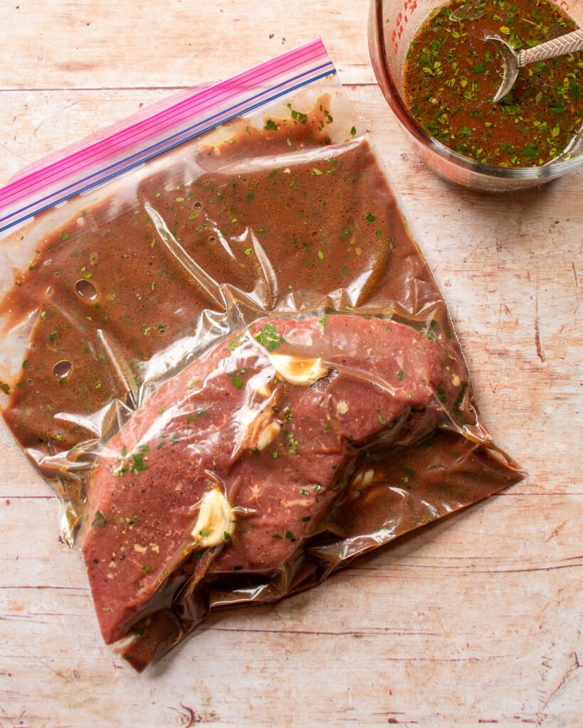 Top round steak marinating in a zipper sealable plastic bag.