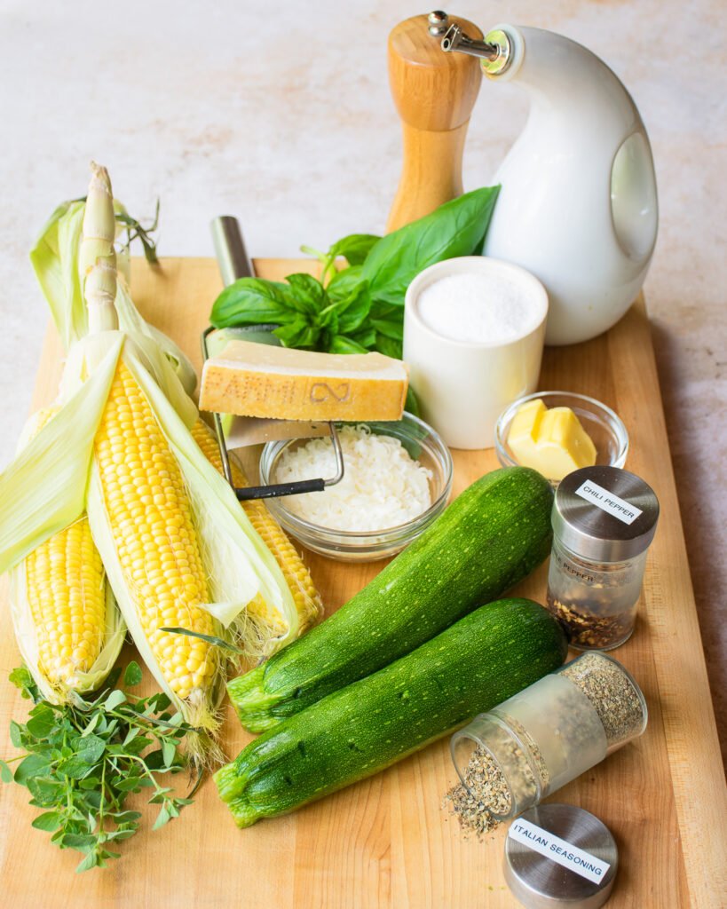 Ingredients on a cutting board - zucchini, corn, butter, parmesan cheese, olive oil, salt, pepper, spices and herbs.