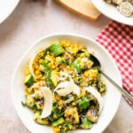 A white bowl of grilled Parmesan Corn and Zucchini on a table with a red and white checkered napkin and other dishes around.