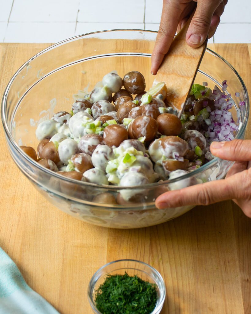 Hands stirring potato salad together.