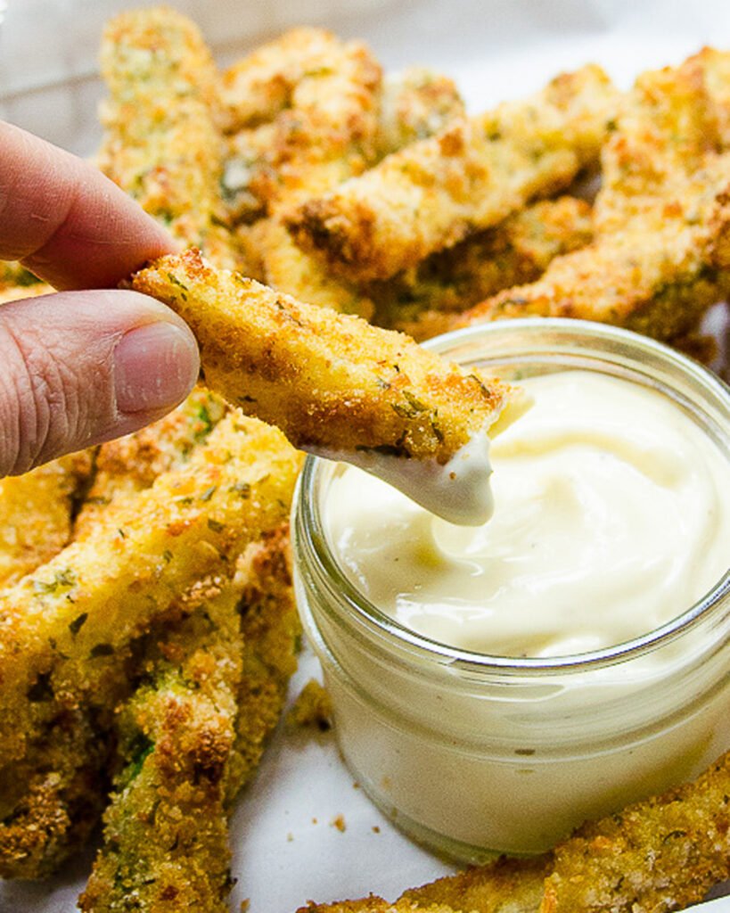 Fingers dipping a zucchini fry into roasted garlic aioli.