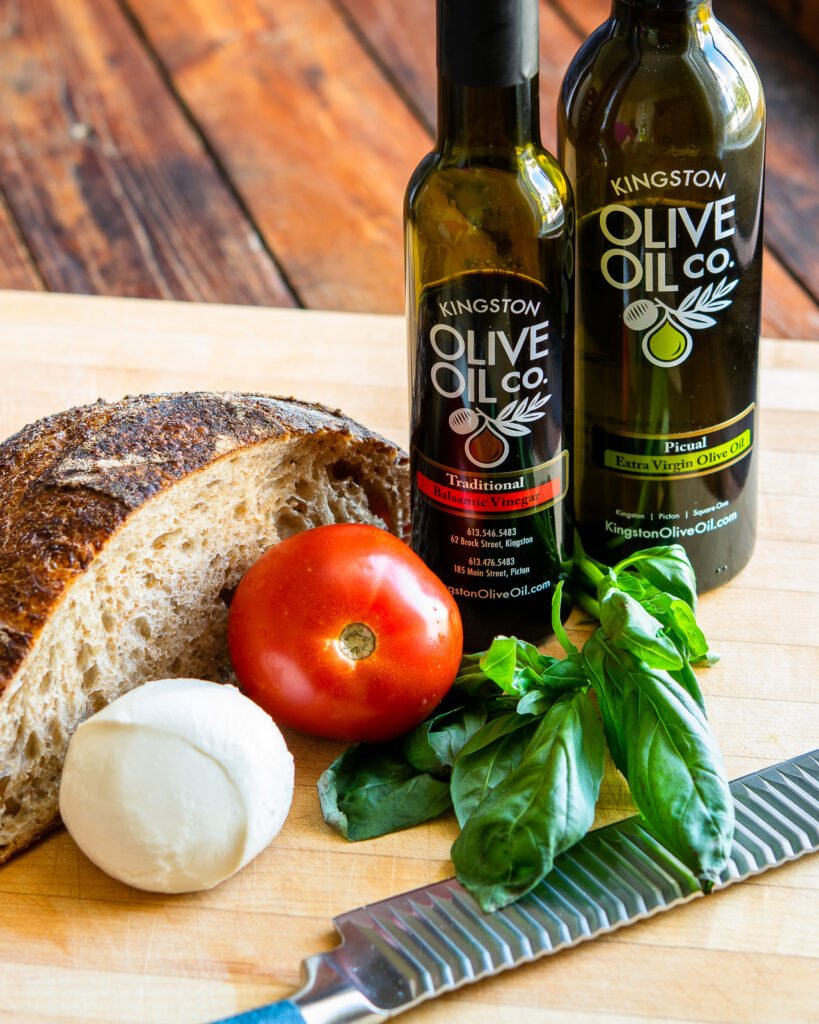 Ingredients on a wooden cutting board - balsamic vinegar, olive oil, bread, mozzarella, tomato and basil.