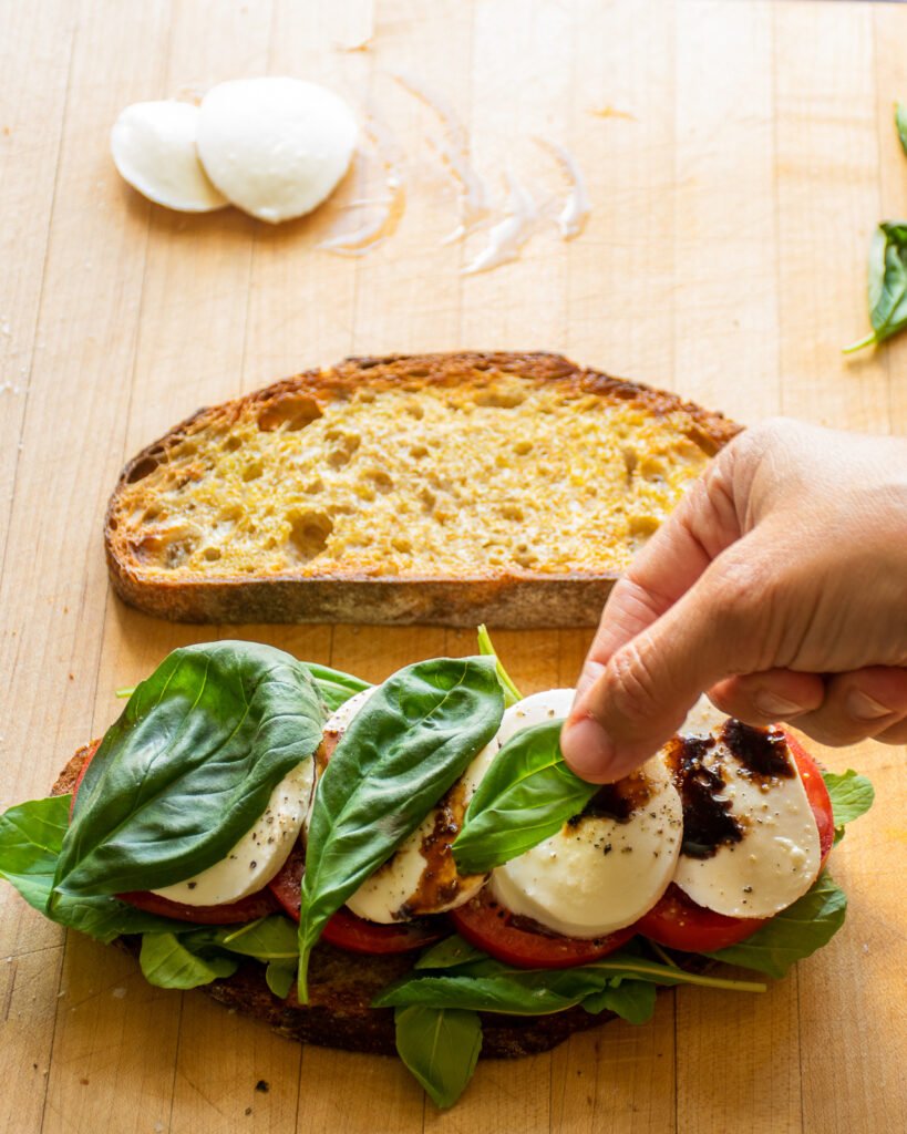 A hand putting a basil leave on top of mozzarella cheese.