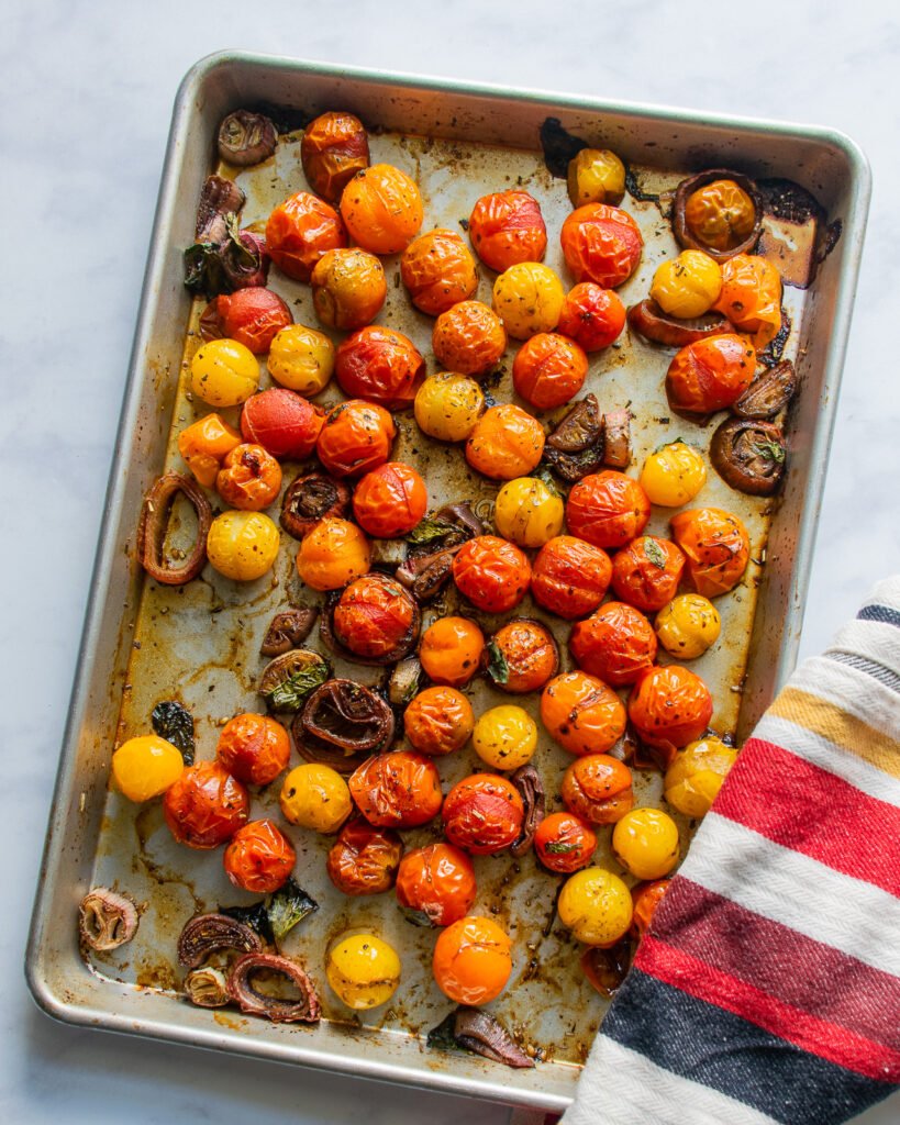 Roasted cherry tomatoes on a sheet pan on a marble counter.