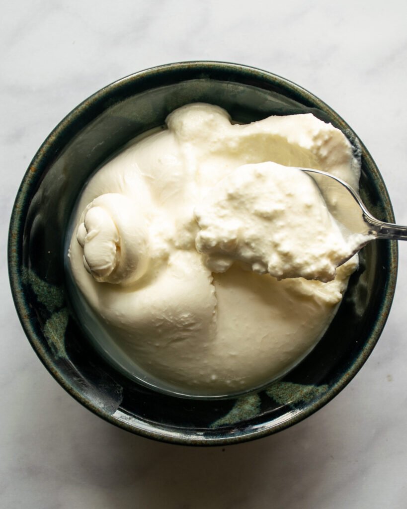 Burrata broken open and being spooned out with a spoon.