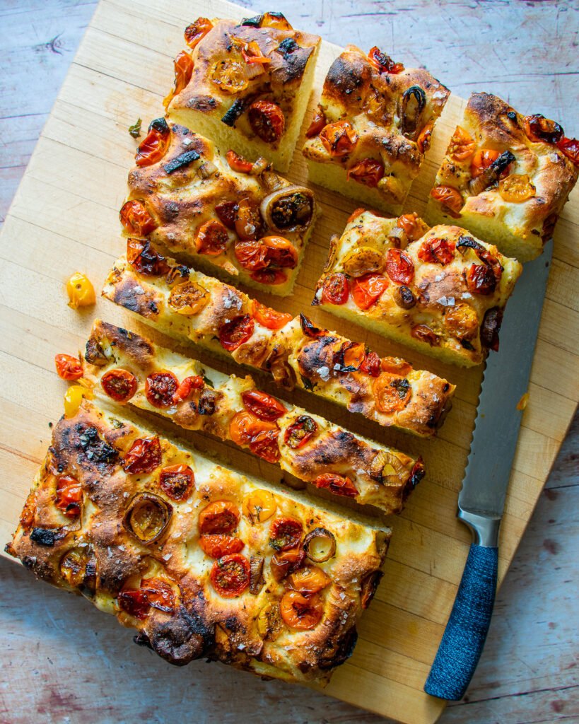 Roasted cherry tomato focaccia bread on a cutting board cut into pieces.