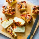 Roasted cherry tomato focaccia bread on a cutting board cut into pieces.