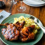 Honey BBQ Grilled Pork Chops on a green platter with mashed potatoes on a wooden table.