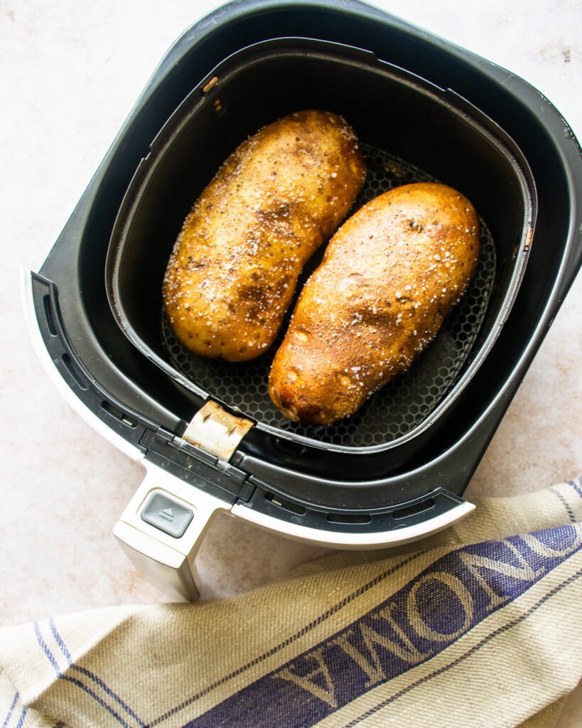 A look down at an air fryer basket with two russet potatoes inside.