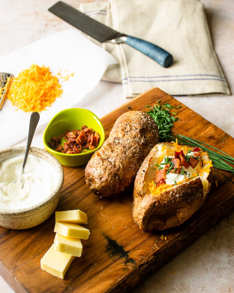 Baked potatoes on a cutting board with toppings surrounding them.