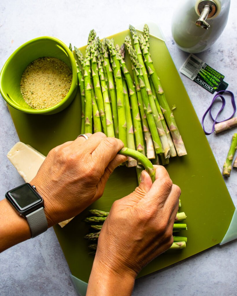 Two hands breaking a spear of asparagus over a green cutting board.