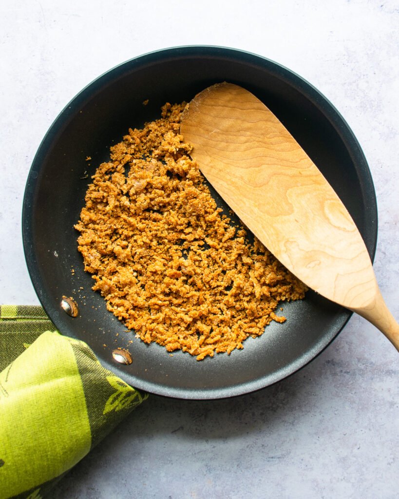 Parmesan Breadcrumbs in a skillet with a green towel and wooden spoon.