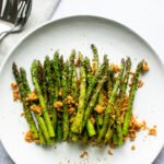 Grilled Asparagus with Crispy Parmesan Breadcrumbs on a white plate with serving utensils nearby.