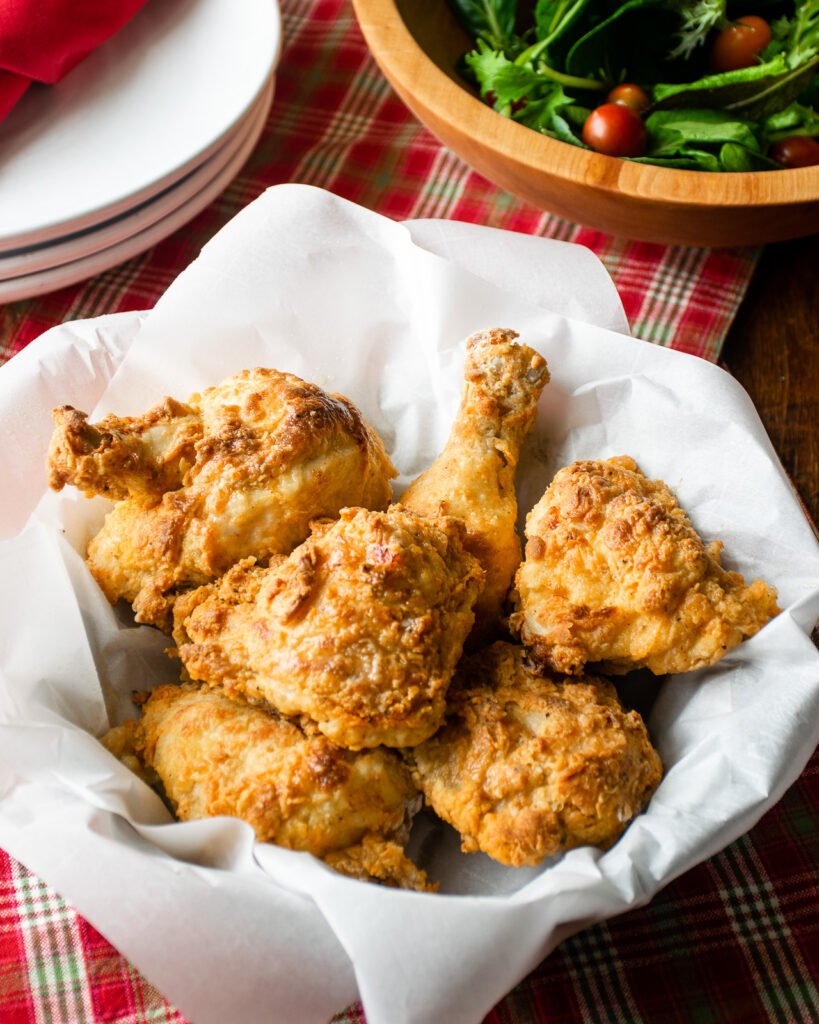AIr Fryer Buttermilk Fried Chicken in a parchment paper lined basket on a red checkered placemat.