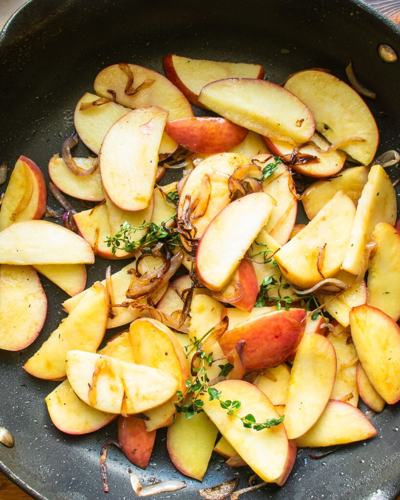 Apples, onion and thyme cooking in a skillet.